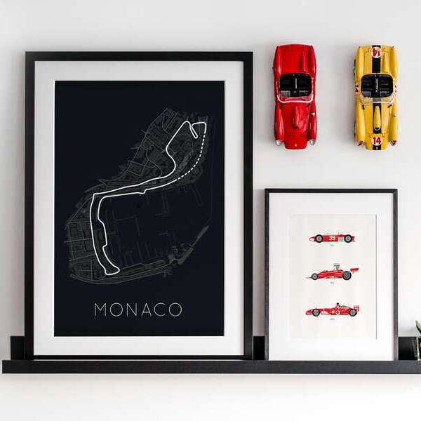 Wall decoration with two diecast racing cars on the wall and two posters on a shelve. The posters are from the monaco gp racing track and the history of ferrari f1 cars.